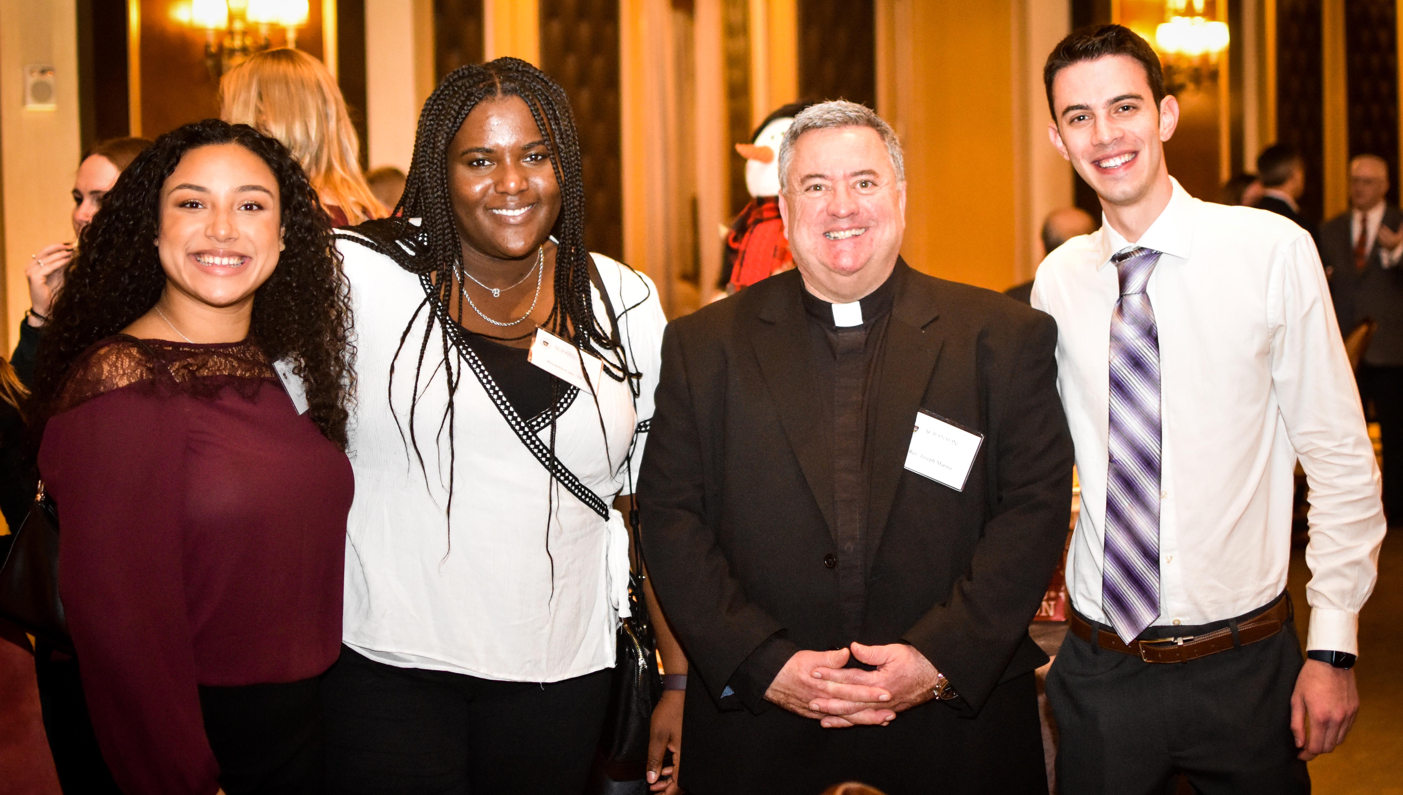 From left, Taylor Roman '21, Breanna Cole '21, the Rev. Joseph G. Marina, S.J., University president, and Jeffrey Colucci '21 celebrate the Christmas season together at the New York Athletic Club Dec. 8. 