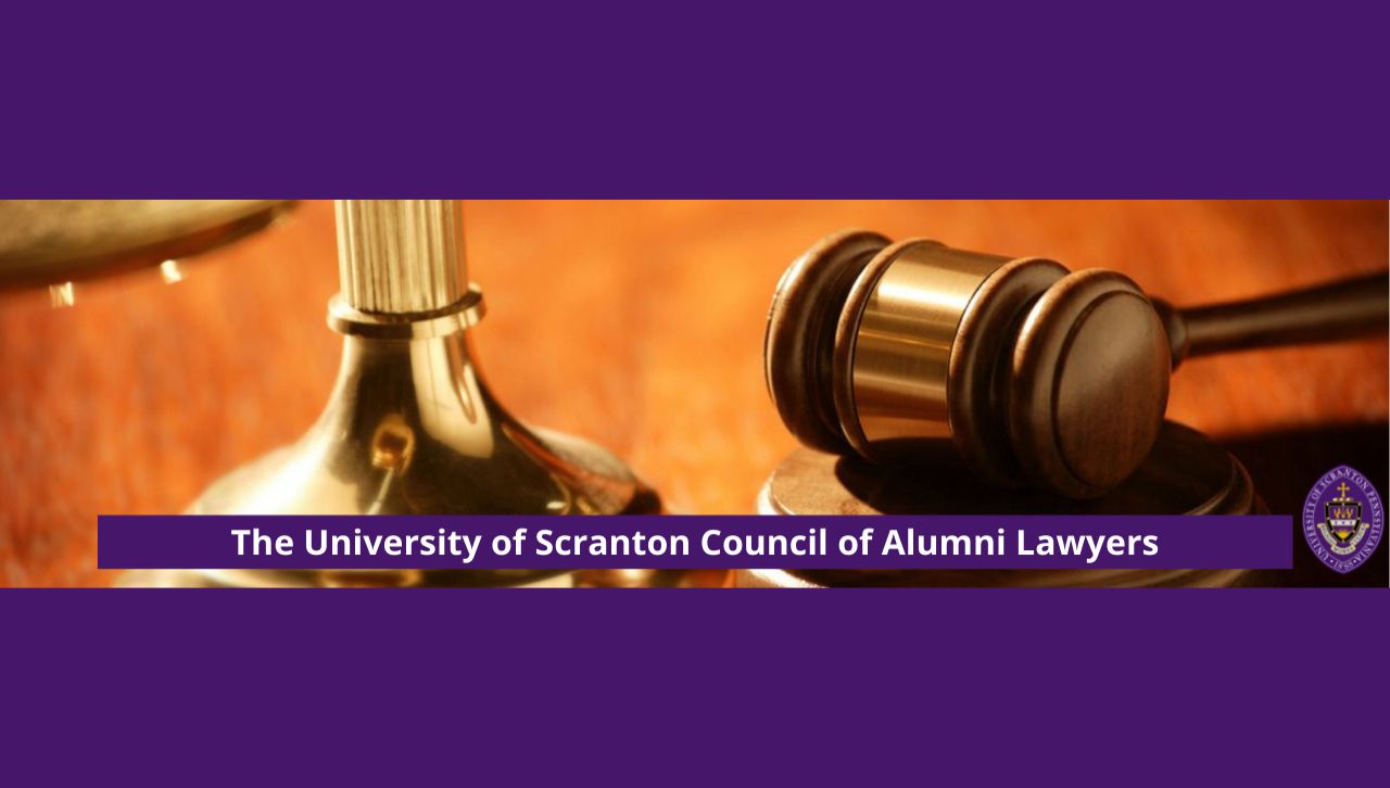 A graphic stating "The University of Scranton Council of Alumni Lawyers" next to the Seal of the University of Scranton" superimposed over a photo of a gavel and a scale sitting atop a wooden desk.