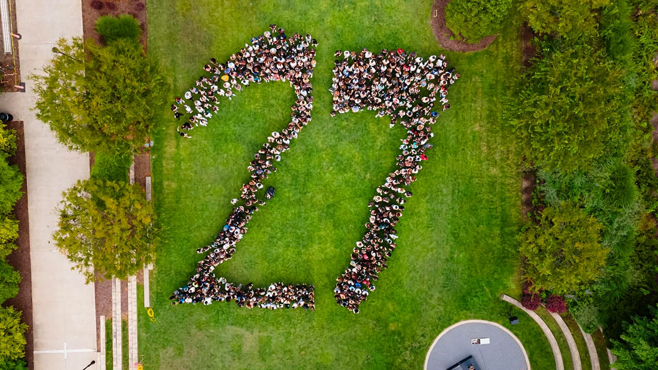 aerial view of students standing in such a way as to form numeral 27 on green lawn