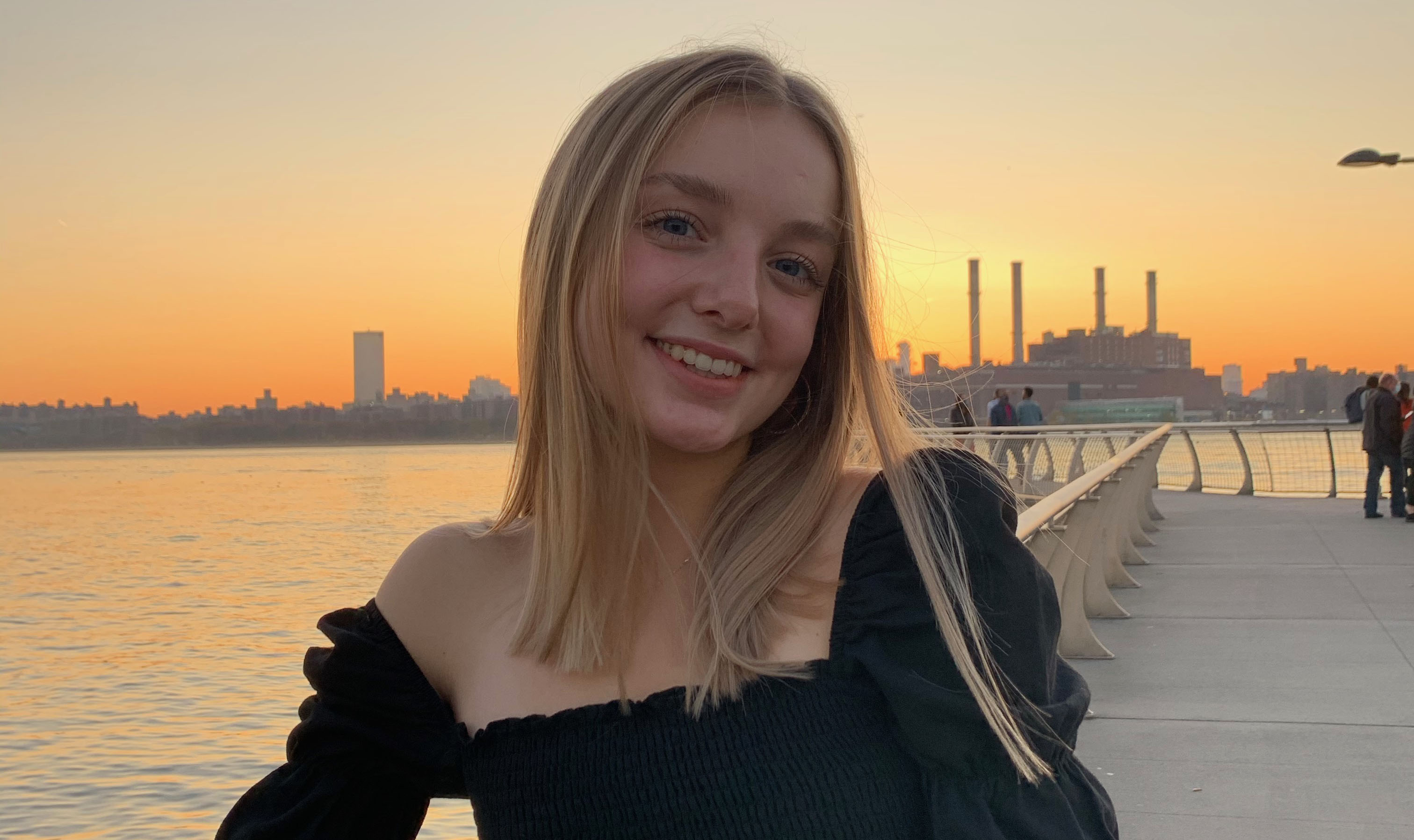 young woman standing on a pier with cityscape and sunset in background